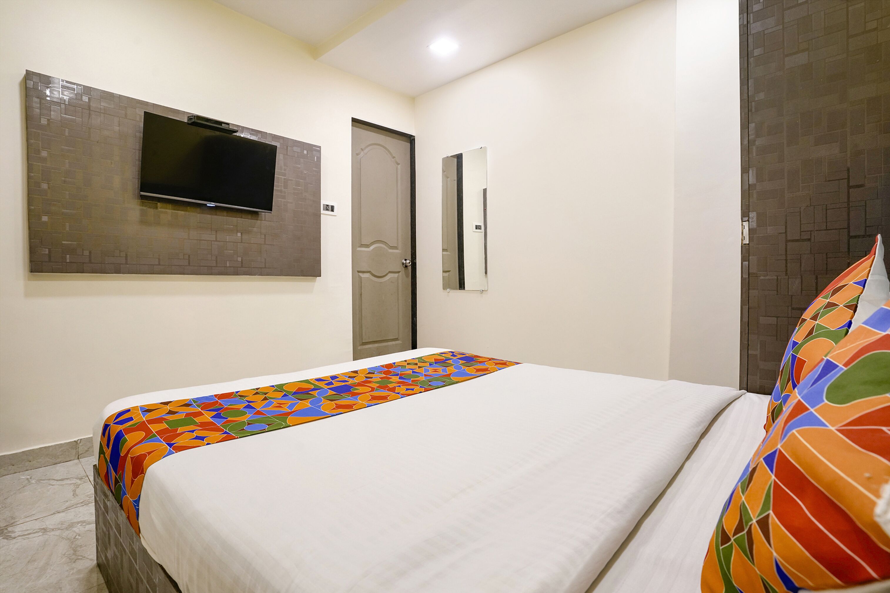 Une chambre d’hôtel comprenant un lit, un téléviseur à écran plat fixé au mur, une porte et un miroir.