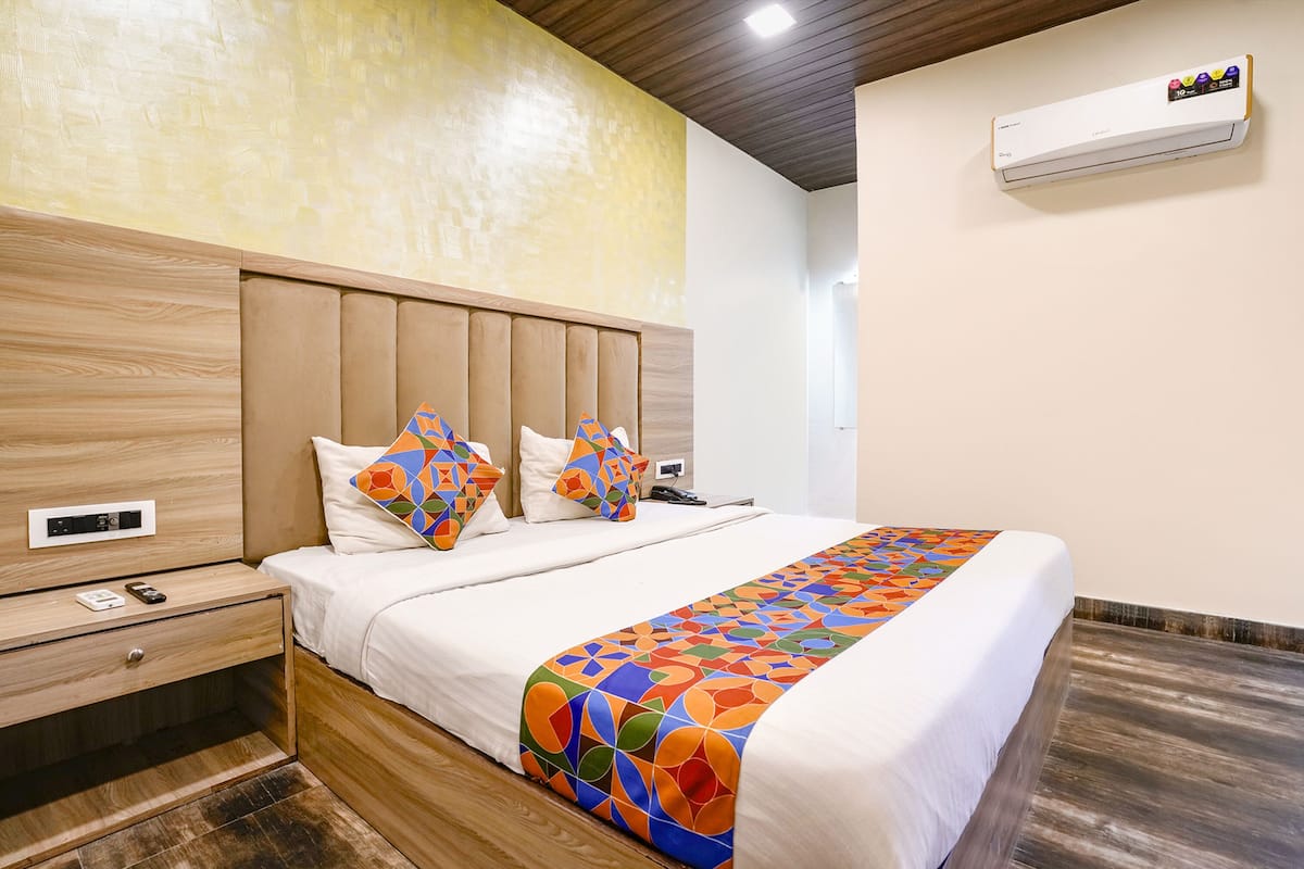 Una habitación de hotel moderna con cabecera de madera, cama con ropa blanca, almohadas coloridas y una manta estampada.
