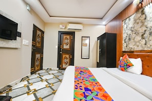 Una habitación de hotel con cama, armario, televisor montado en la pared y aire acondicionado.
