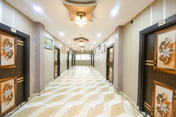 A hotel corridor with a patterned floor, decorative doors, and a ceiling with recessed lighting.