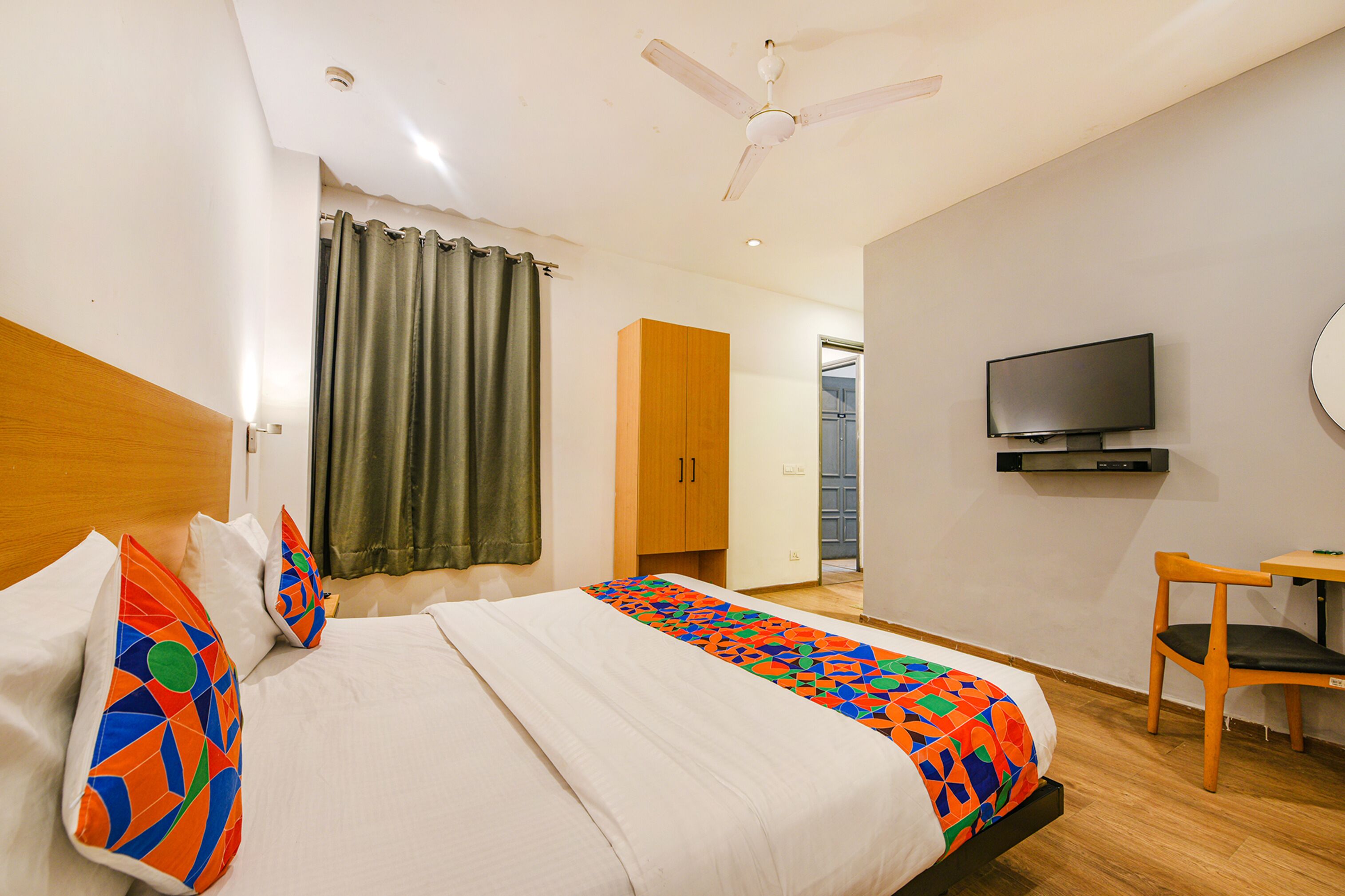 A hotel room with a bed, a television, a ceiling fan, and a wooden chair.