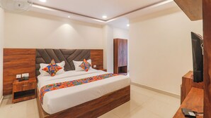 A modern bedroom with a wooden headboard, a bed with colorful geometric pillows, a bedside table with a phone and charger, and a wooden wardrobe. - Fabhotel Rachna Palace And Banquets (Lucknow)