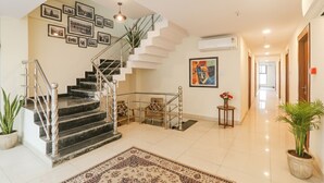 A spacious foyer with a marble floor, a staircase with metal railings, and a hallway leading to a door. - Fabhotel Rachna Palace And Banquets (Lucknow)