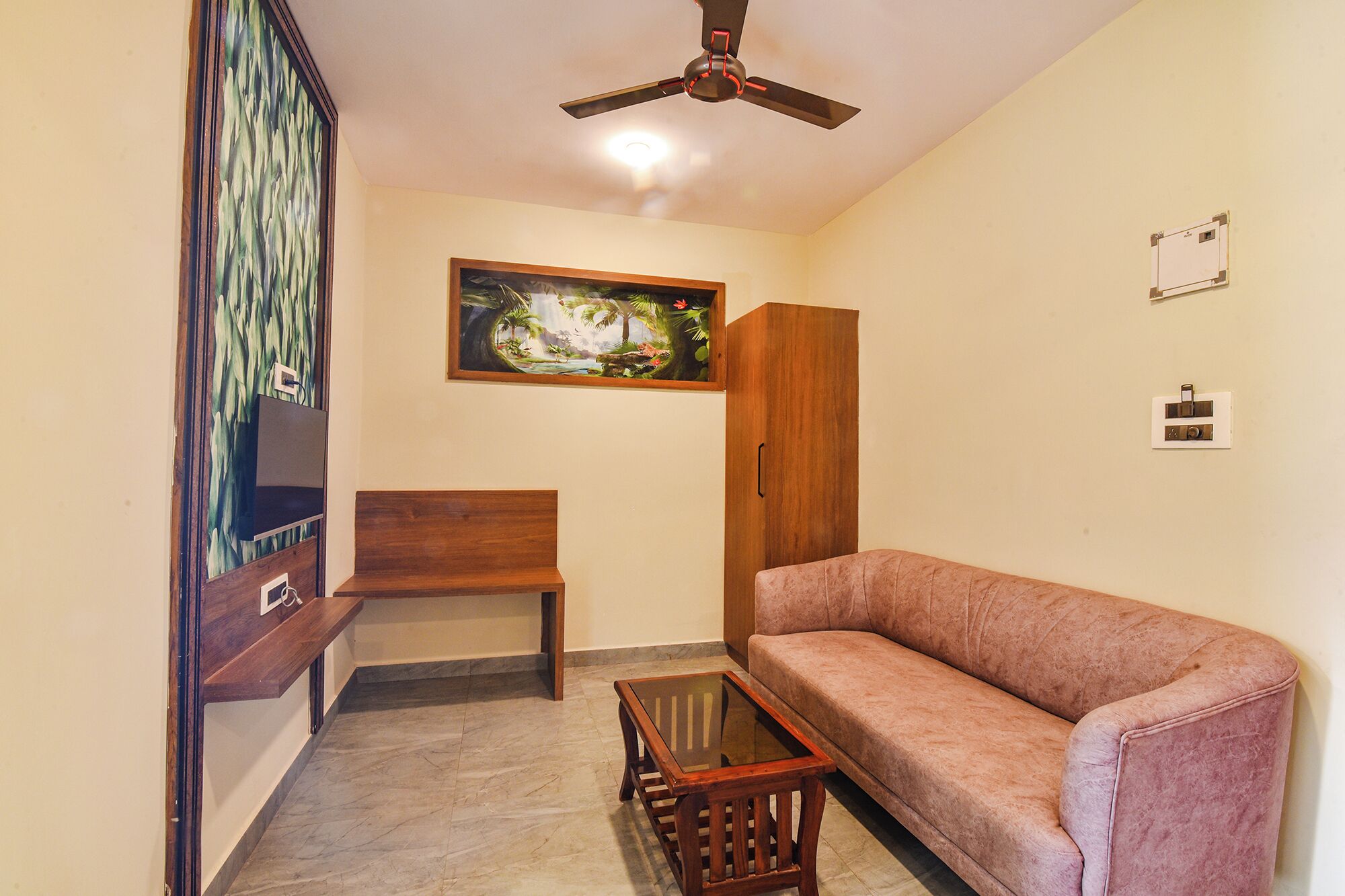 A living room with a sofa, a glass-top coffee table, a wooden bench, a ceiling fan, a painting on the wall, and a cabinet.