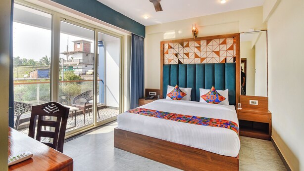 A hotel room with a large bed, a ceiling fan, a balcony with a view of buildings, and a desk with a chair. - FabHotel Jingle Tree Resort Nr Arambol Beach (Arambol)