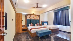 A hotel room with two beds, a wooden wardrobe, a blue bench, a ceiling fan, and a large window with curtains. - FabHotel Jingle Tree Resort Nr Arambol Beach (Arambol)