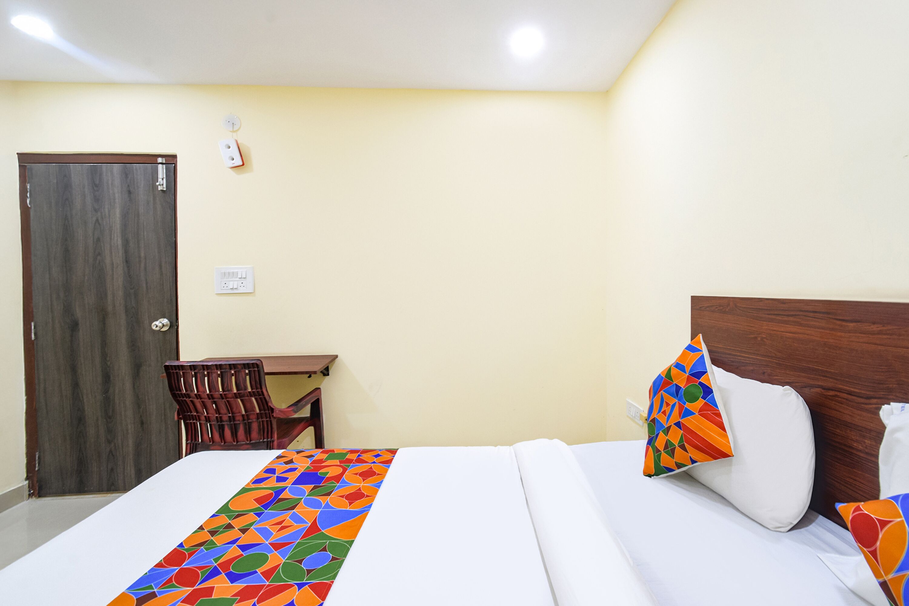 A hotel room with a bed, a wooden headboard, a desk, and a chair.