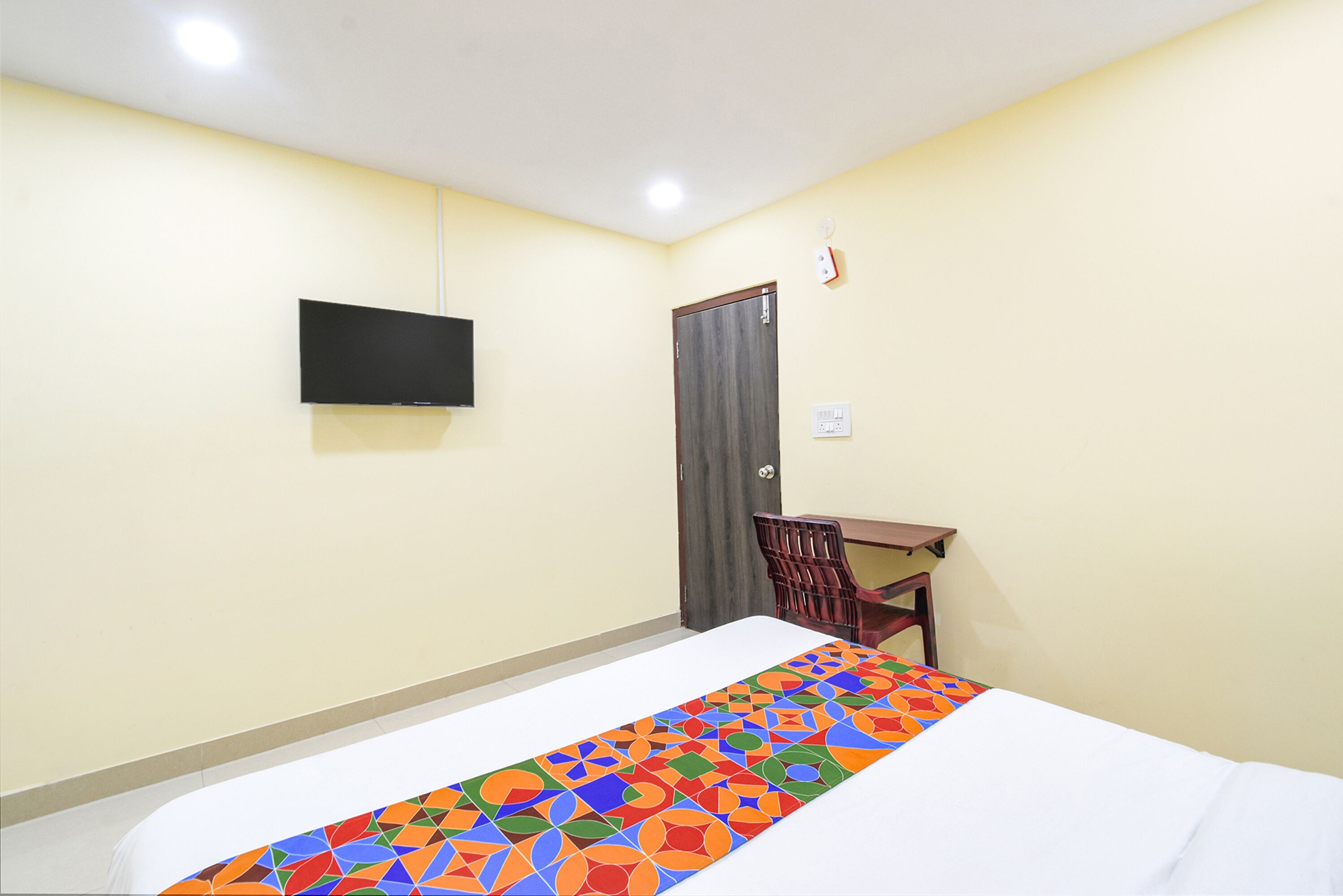 A hotel room with a bed, a desk, a chair, a television, and a door.