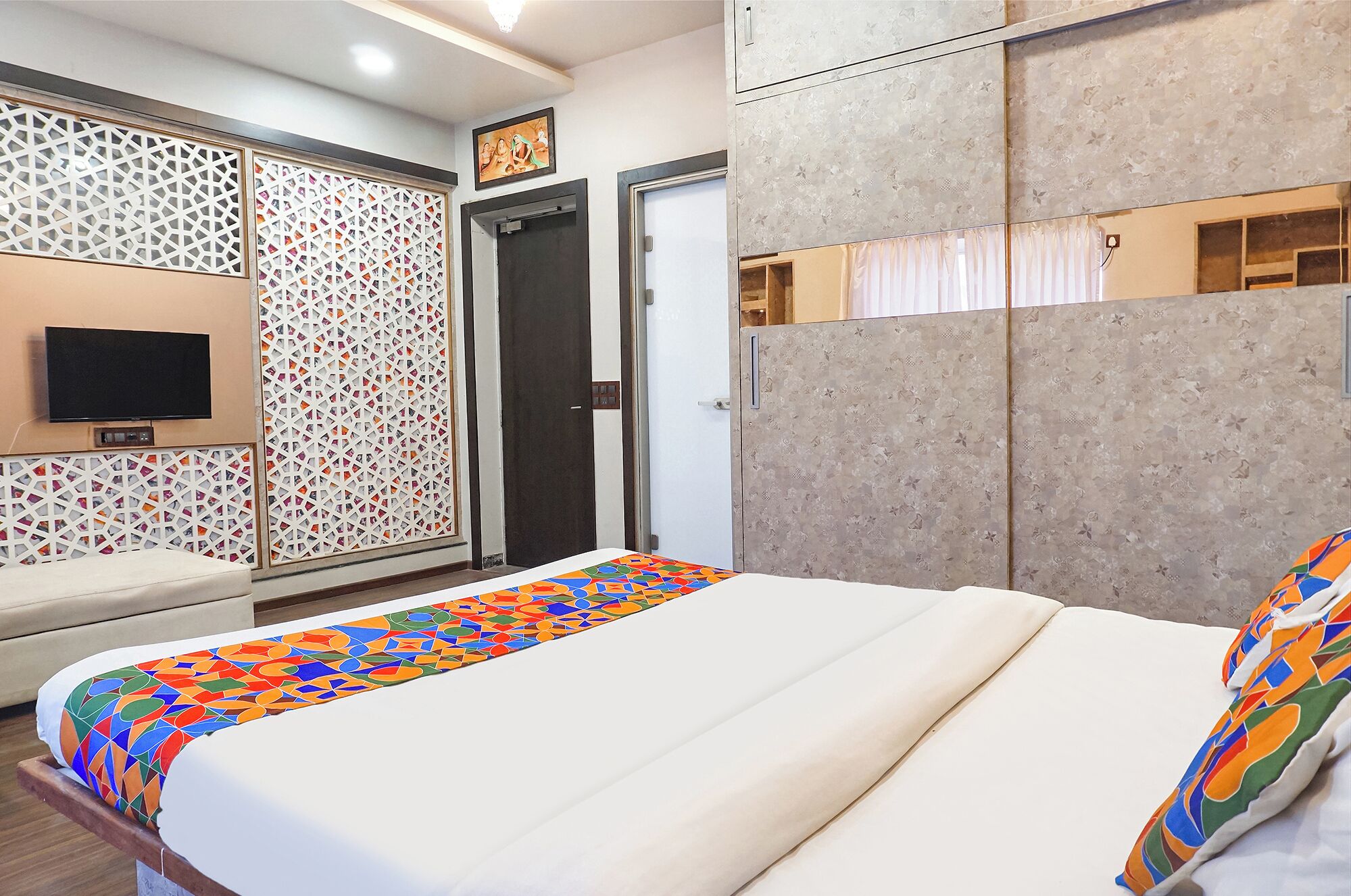 A hotel room with a bed, a TV mounted on the wall, and a wardrobe with a mirror.