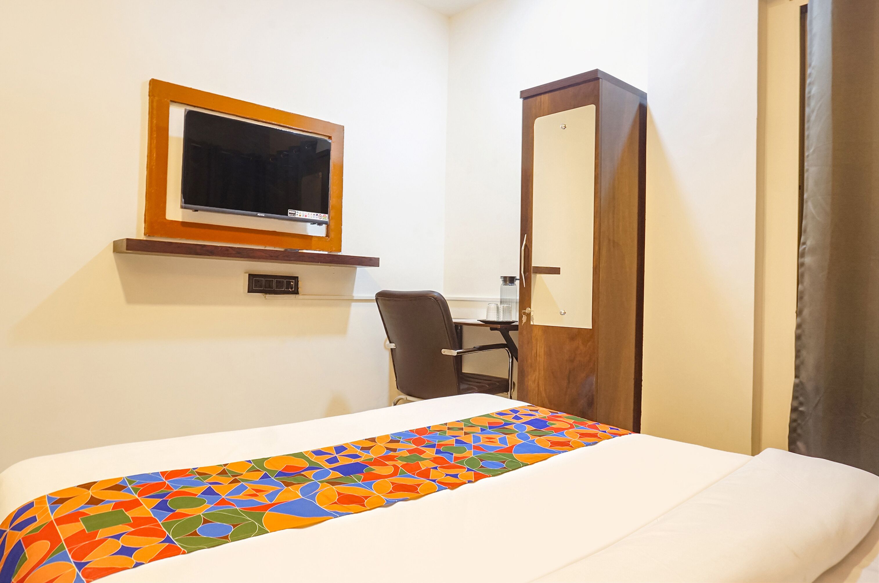 A hotel room with a bed, a desk, a chair, a TV, and a wardrobe.