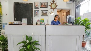 Un comptoir d’accueil avec une personne assise derrière, entourée de tableaux encadrés, d’une horloge décorative et de plantes en pot.