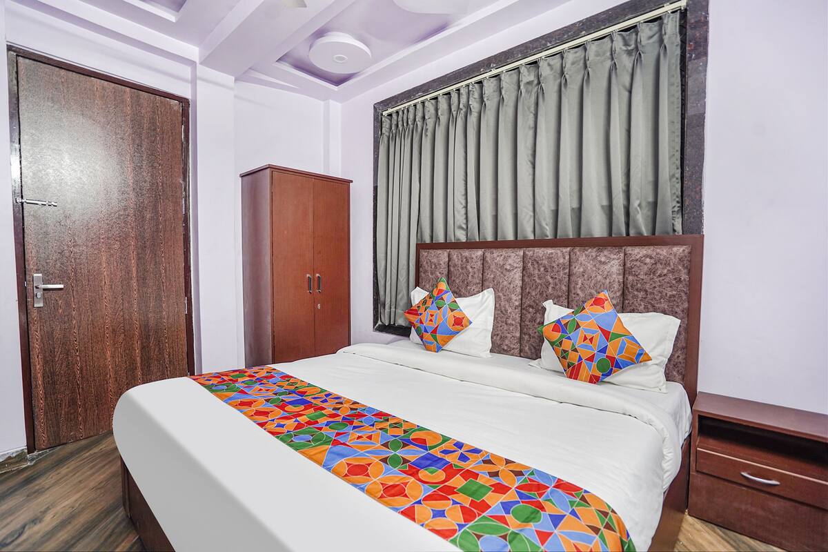 Une chambre d’hôtel bien rangée, avec un grand lit, une armoire en bois et une fenêtre avec des rideaux.