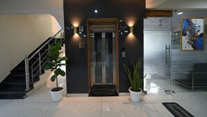A modern building entrance with a staircase, two potted plants, an elevator, and a glass door. - Fabhotel Palm Paradise (Noida)