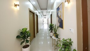 A hotel hallway with a polished floor, potted plants, and wall-mounted lighting fixtures. - Fabhotel Palm Paradise (Noida)