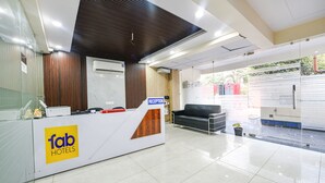 A hotel reception area with a reception desk, a couch, and a potted plant. - Fabhotel Palm Paradise (Noida)