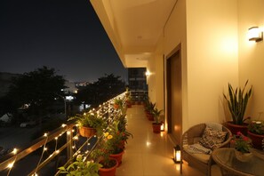 A balcony with potted plants, string lights, and a wicker chair. - Fabhotel Palm Paradise (Noida)