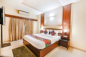 A hotel room with a large bed, a nightstand, an air conditioning unit, and a television. - FabHotel Shreyas Shack (Bengaluru)