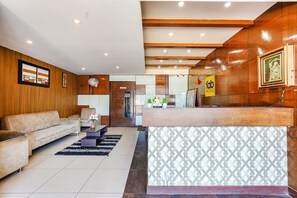 A hotel lobby with a reception desk, a sofa, a coffee table, and a fan. - FabHotel Shreyas Shack (Bengaluru)