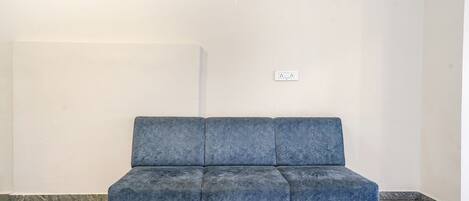 A blue sofa in a corner of a room with white walls and a marble floor.