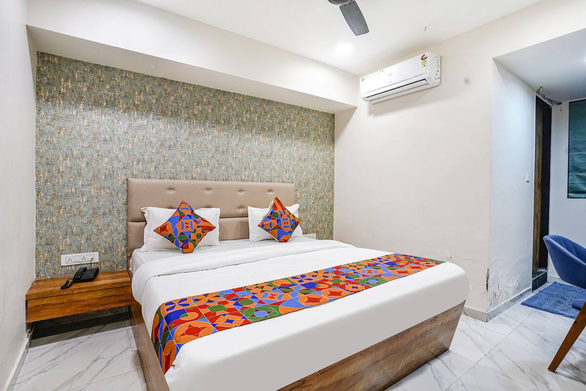 A modern hotel room with a large bed, a headboard, a nightstand, an air conditioning unit, and a blue chair.