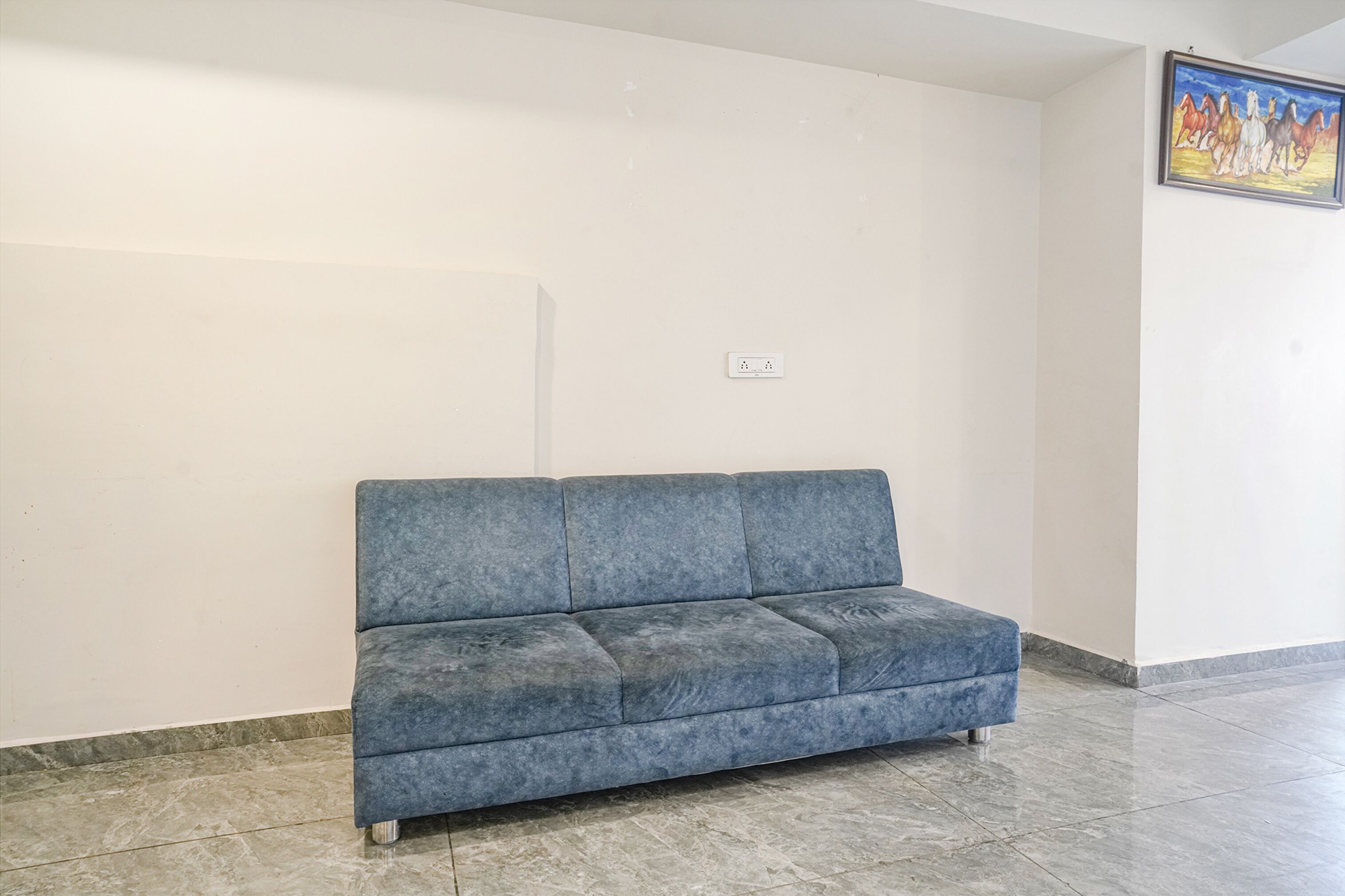 A blue sofa in a room with a tiled floor and a plain wall.