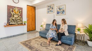 Un espace d’accueil avec un canapé bleu, une porte en bois et deux œuvres d’art encadrées accrochées au mur.