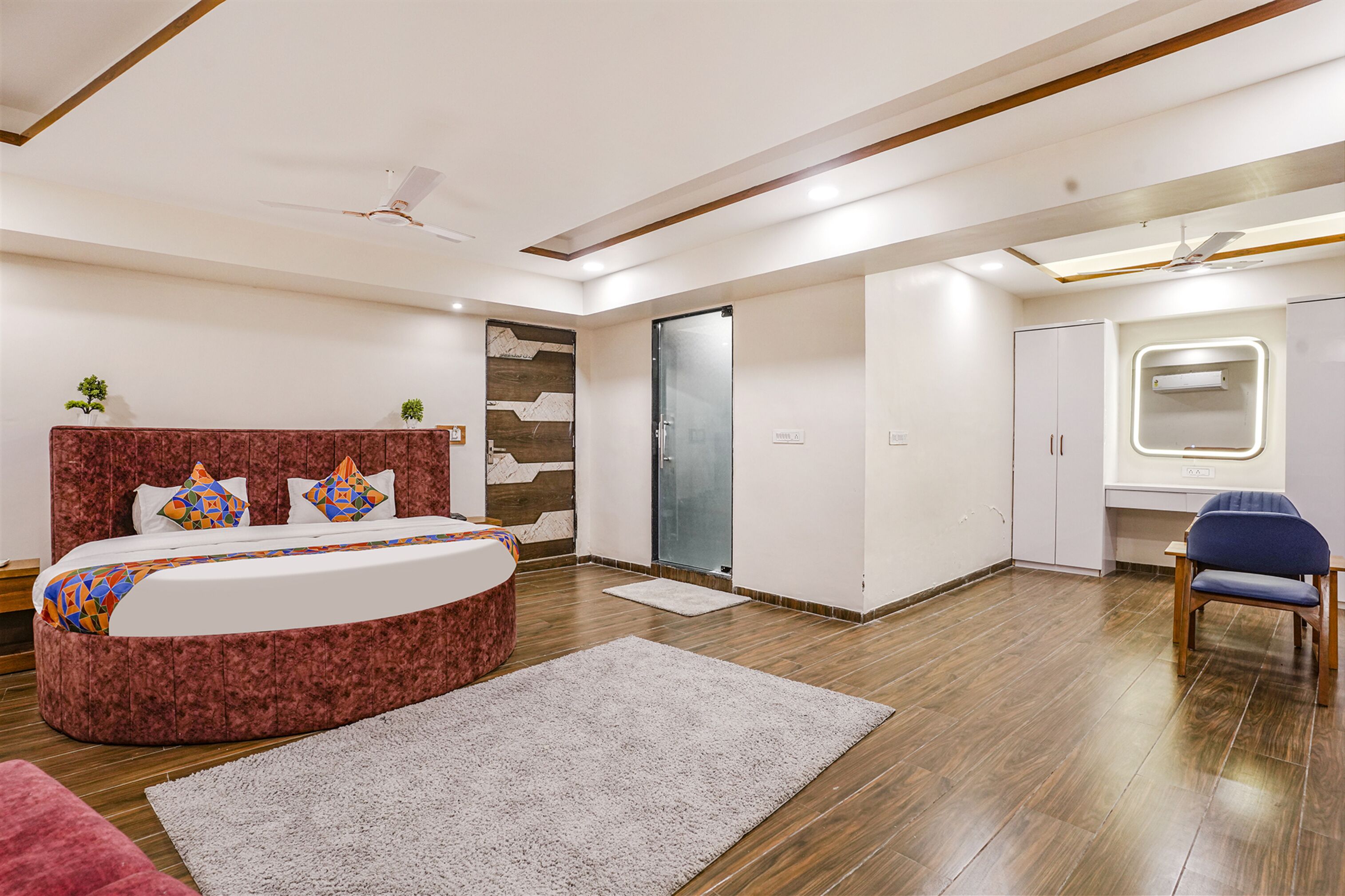 A modern bedroom with a curved bed, a wooden floor, a ceiling fan, and a small desk with a chair.