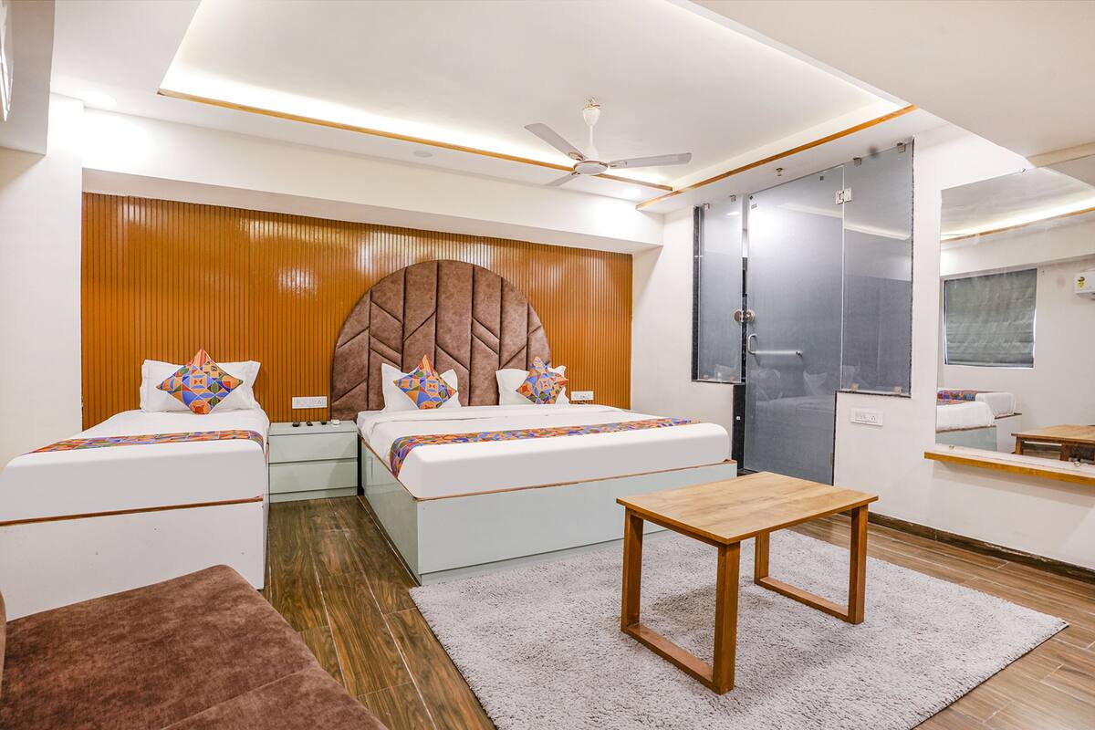 A modern hotel room with two beds, a wooden headboard, a small table, and a mirror.