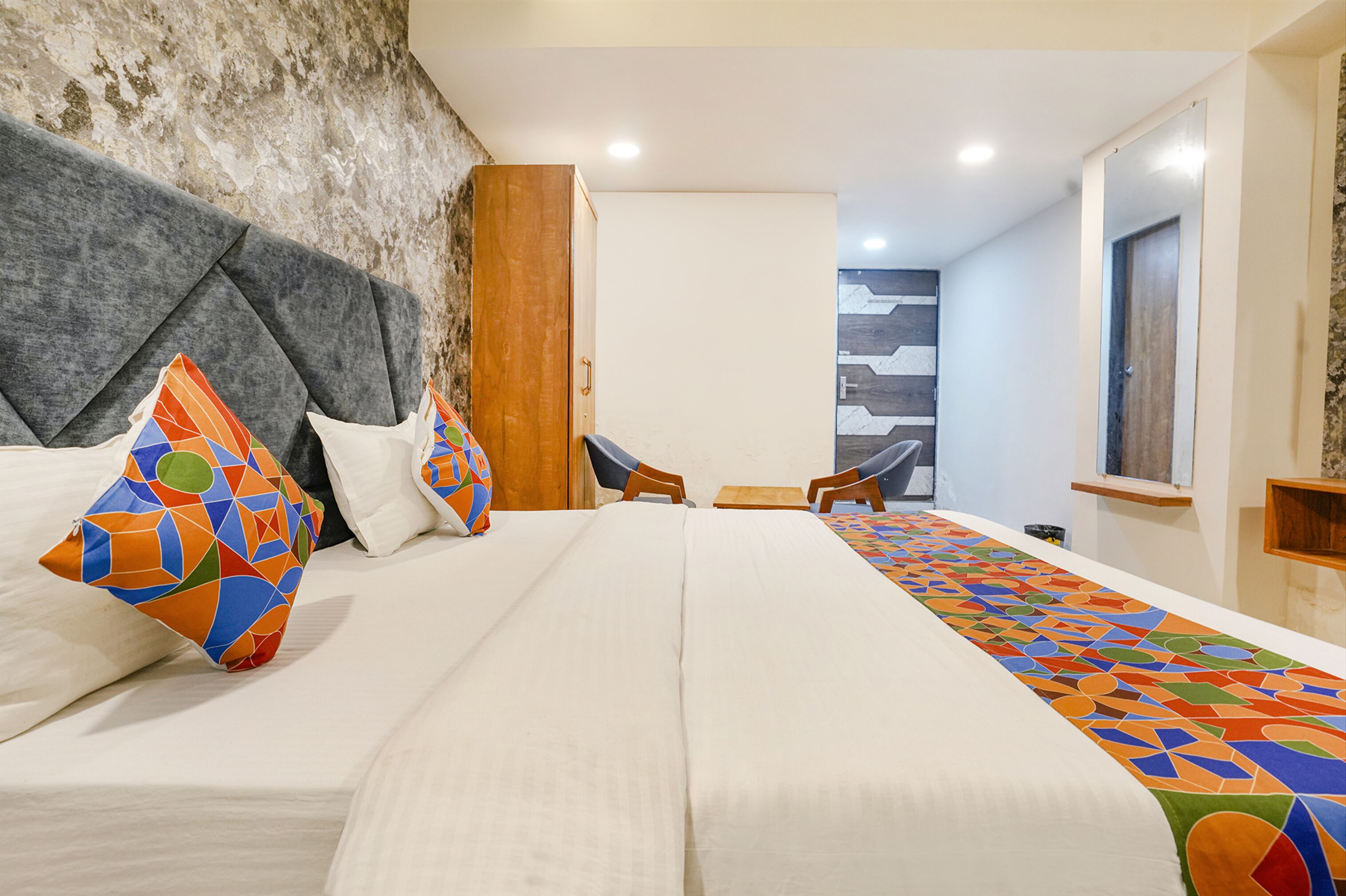A hotel room with a large bed, a wooden headboard, a small table, and a chair.