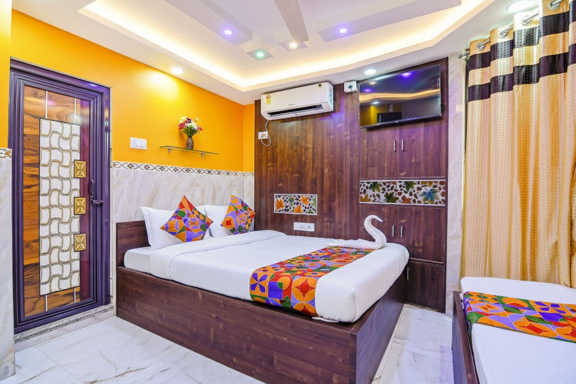 A hotel room with a bed, a TV, an air conditioning unit, and a shower curtain.