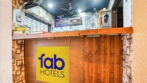 Egy fából készült recepciós pult, rajta egy „fab hotels” felirattal, egy „Harshita Inn” táblával és egy mennyezeti ventilátorral.