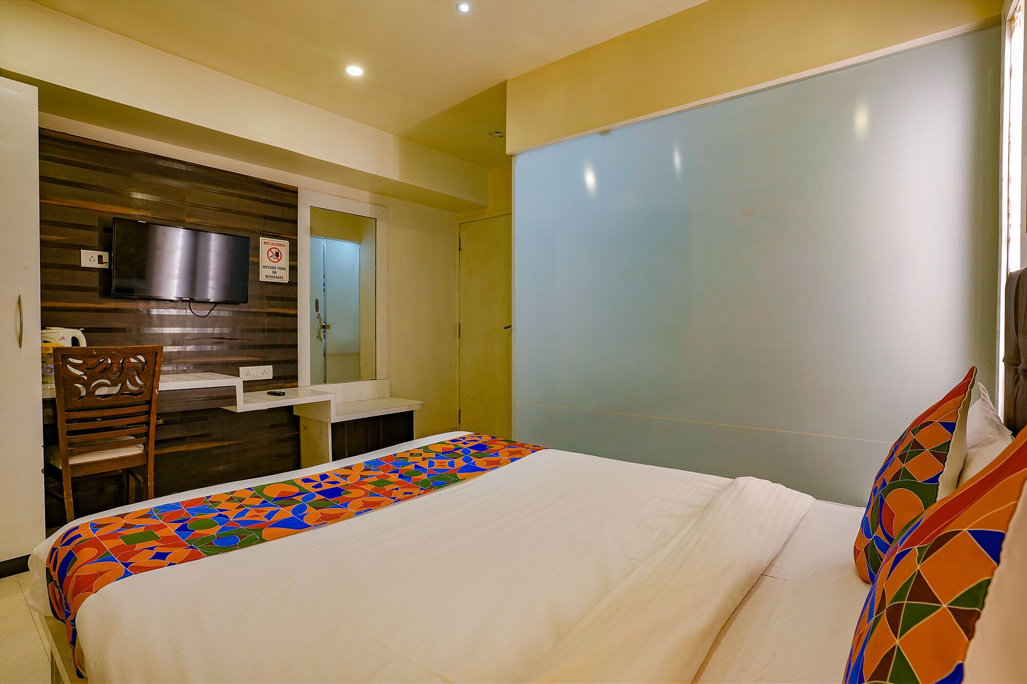 A hotel room with a bed, a desk, a chair, a television, and a wardrobe.