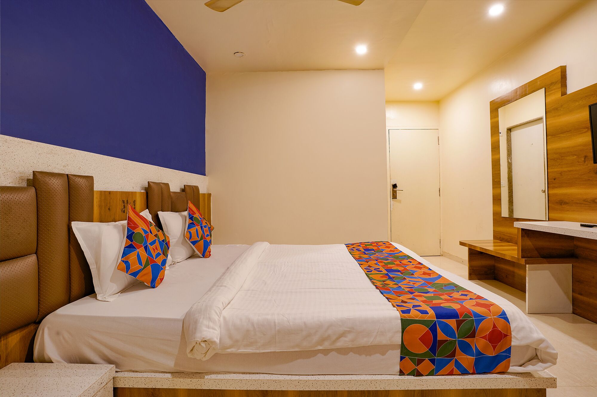 A hotel room with a large bed, a wooden headboard, and a colorful geometric-patterned bed runner.