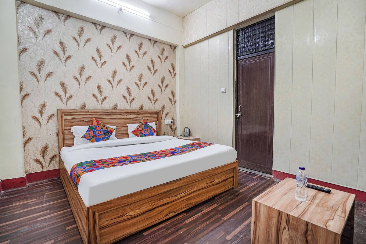 A room with a wooden bed, patterned wallpaper, a wooden door, and a small wooden table with a water bottle.