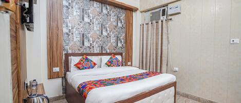 A neatly made bed with a patterned headboard, a kettle on a wooden table, and an air conditioning unit on the wall.