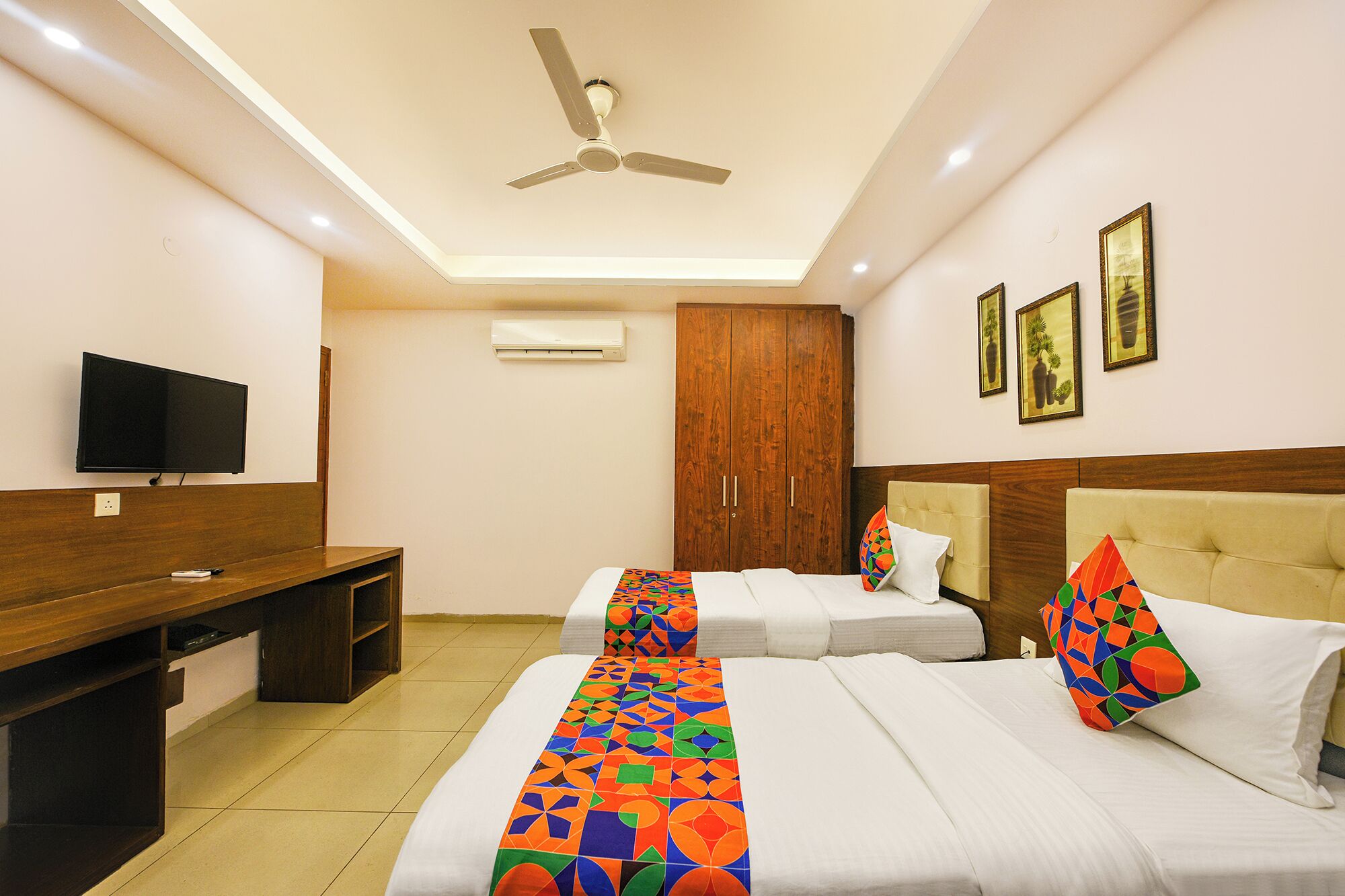 A hotel room with two beds, a TV, a wardrobe, and a ceiling fan.