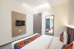 A modern hotel room with a large bed, a flat-screen TV mounted on the wall, a wooden door, and a mirror reflecting the room. - Fabhotel Mahalaxmii Grand (Kanpur)
