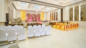 A banquet hall with rows of white and yellow chairs, a stage with floral decorations, and chandeliers. - Fabhotel Mahalaxmii Grand (Kanpur)