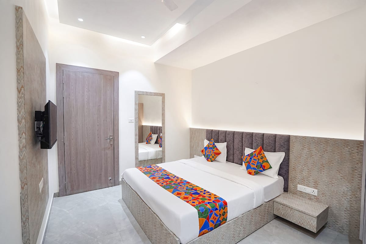 A modern hotel room with a large bed, a small bedside table, a TV mounted on the wall, and a mirror above the bed.