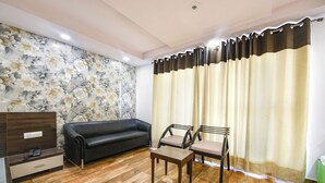 A living room with a floral wallpaper, a black sofa, two chairs, a wooden coffee table, and a wooden cabinet with a telephone. - Fabhotel Angel Green Residency (Gurugram)