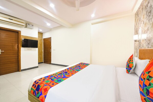 A hotel room with a bed, a TV, a wooden door, and a patterned rug.