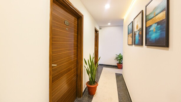 A hallway with wooden doors, potted plants, and framed artwork on the walls. - Fabhotel Angel Green Residency (Gurugram)