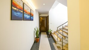 A hallway with three framed artworks, a potted plant, and a staircase with metal railings. - Fabhotel Angel Green Residency (Gurugram)