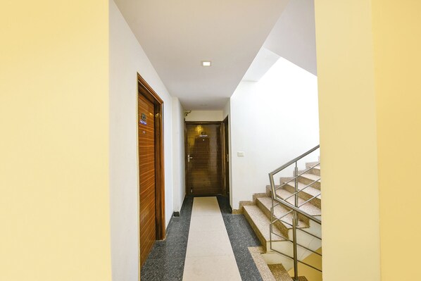 A narrow hallway with wooden doors on one side and a staircase with metal railings on the other. - Fabhotel Angel Green Residency (Gurugram)