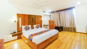 A spacious bedroom with a large bed, wooden headboard, a ceiling fan, and a view of the outdoors through curtains. - Fabhotel Prime Seven Lake View (Hyderabad)