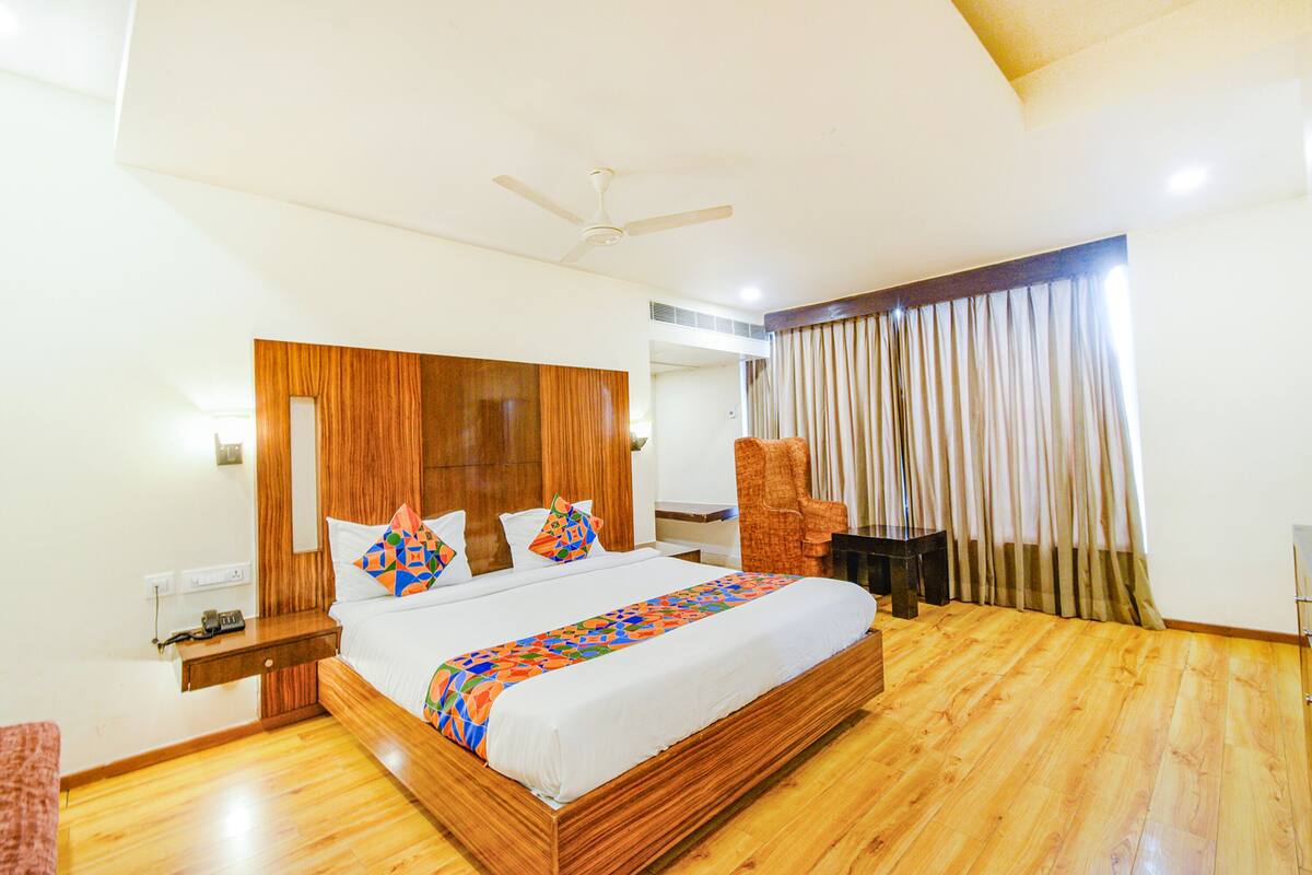 A spacious bedroom with a large bed, wooden headboard, a ceiling fan, and a view of the outdoors through curtains.