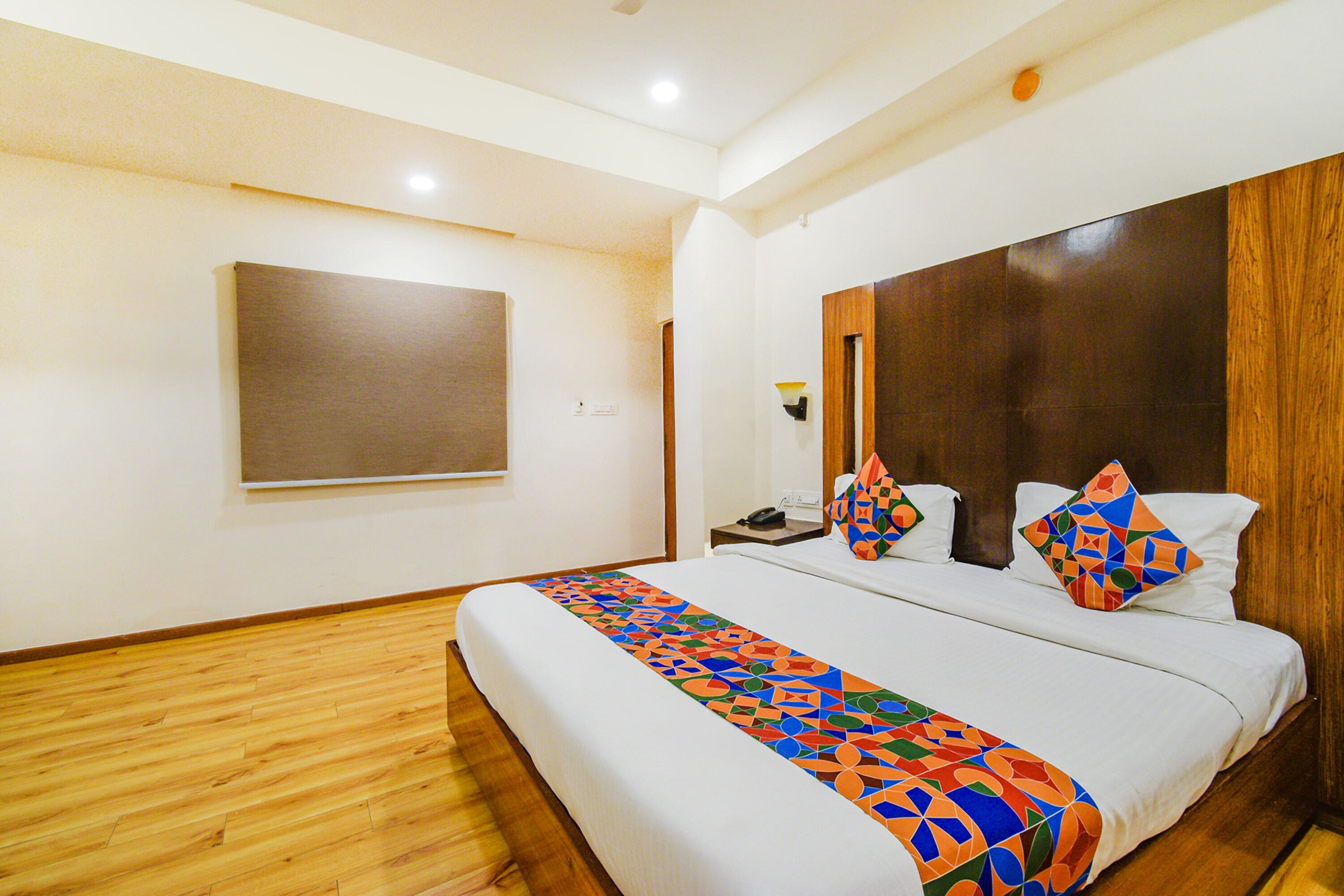 Una habitación de hotel con una cama grande, piso de madera, una televisión montada y un cabecero de madera.