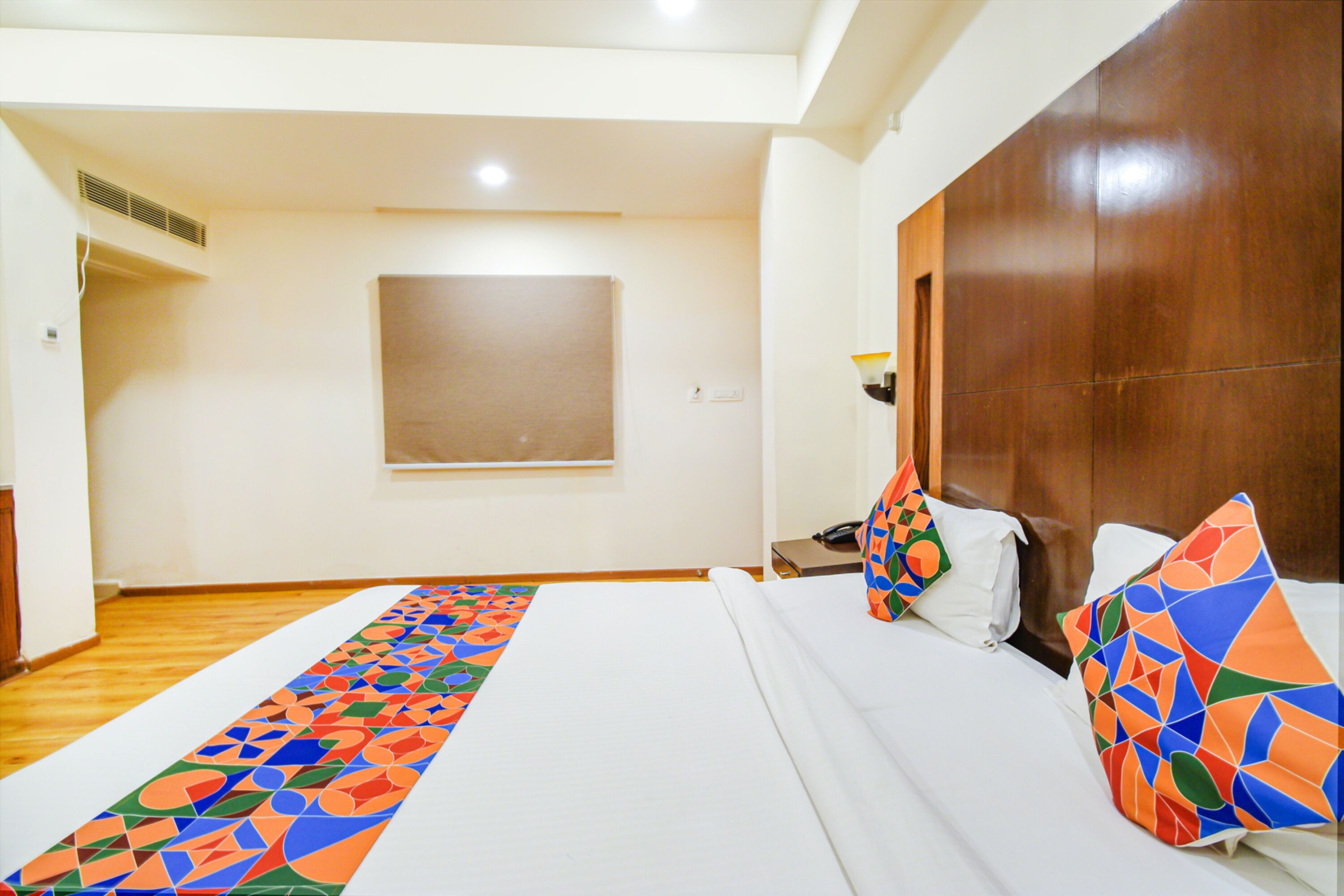 Una habitació d'hotel amb un llit gran, un panell de fusta al capçal i un corredor de colors al terra.