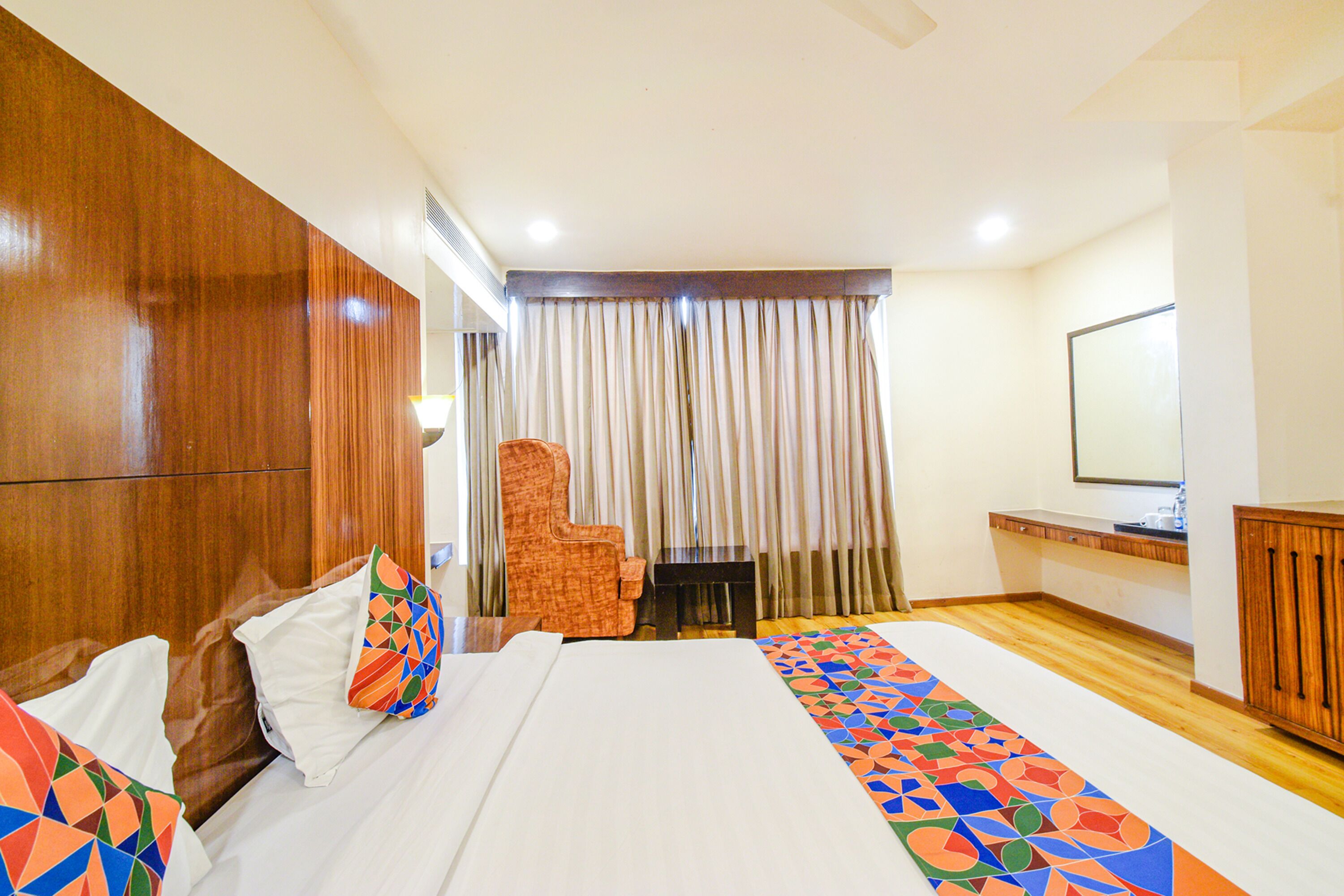 A hotel room with a large bed, a wooden wardrobe, a small table, a chair, and a television.