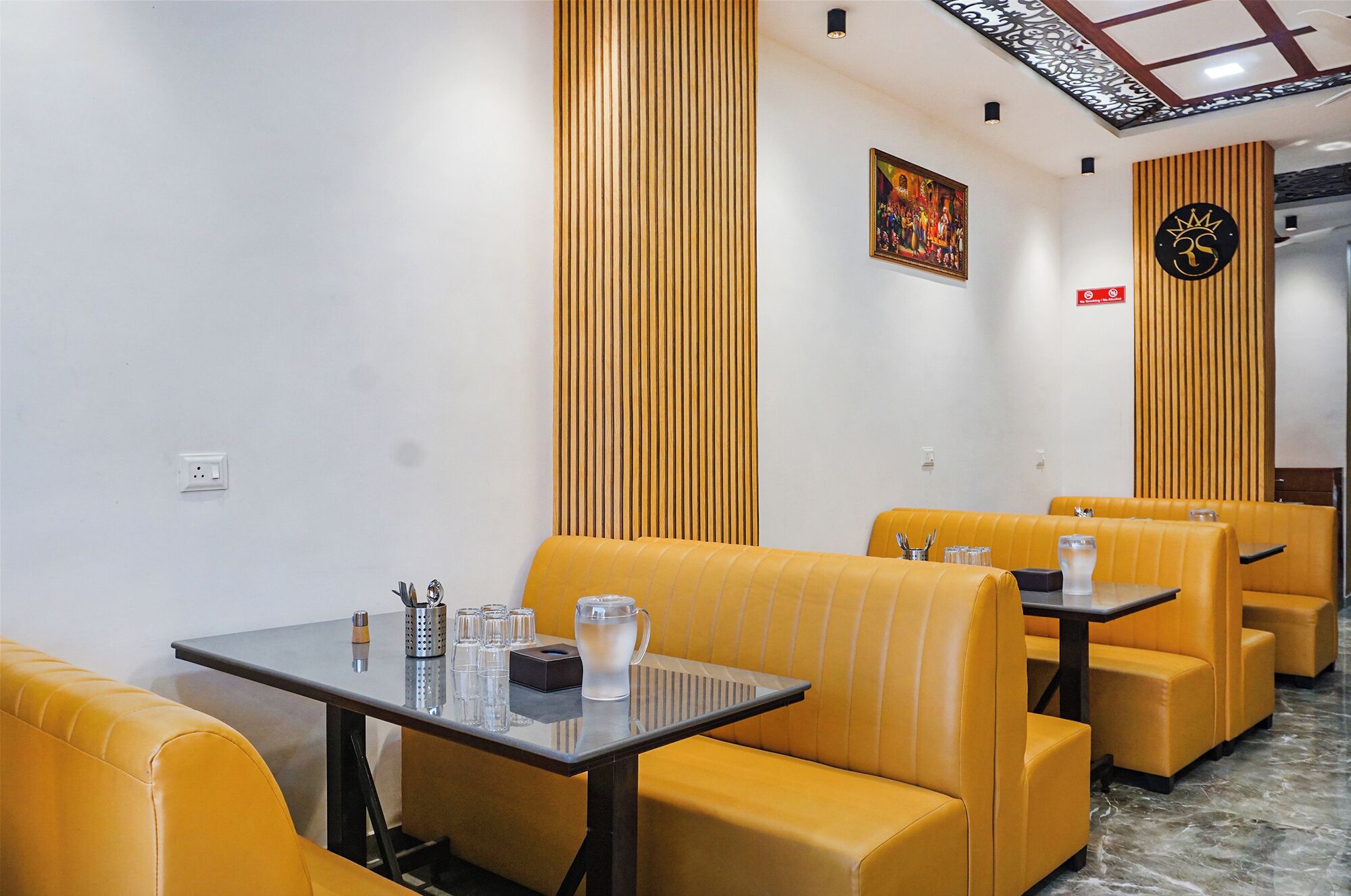 Un restaurante con asientos y mesas amarillas, un cuadro en la pared y un letrero con un símbolo de corona.